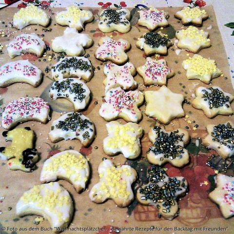 Auf dem Tisch liegen auf Backpapier viele mit Zuckerdekor bunt geschmückte Kekse.
