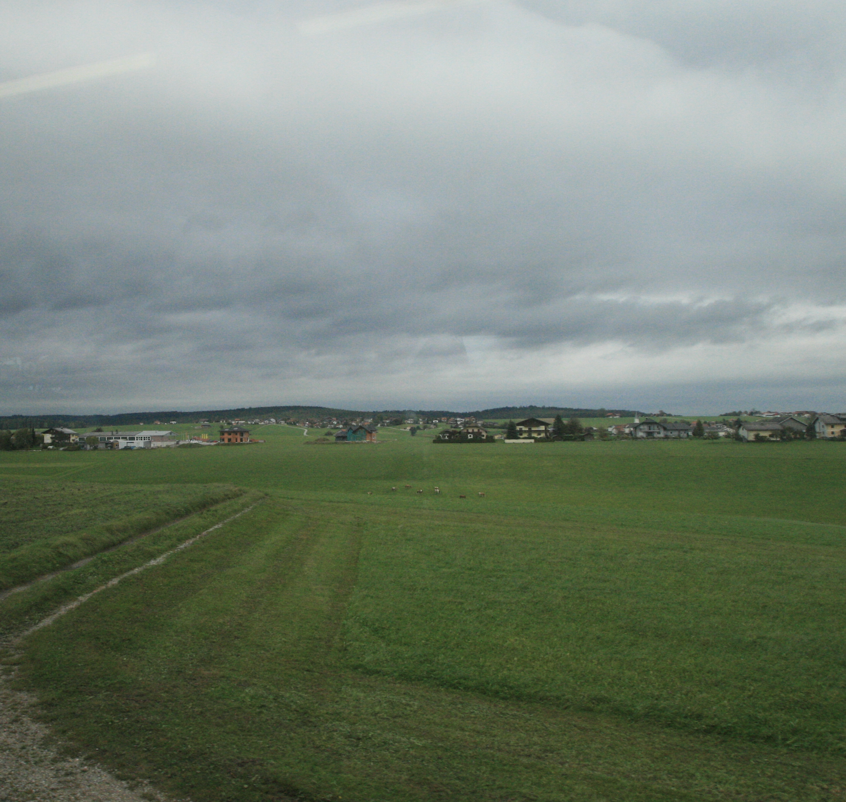 an expansive view from the train of verdant countryside, with houses in the distance, under a grey sky