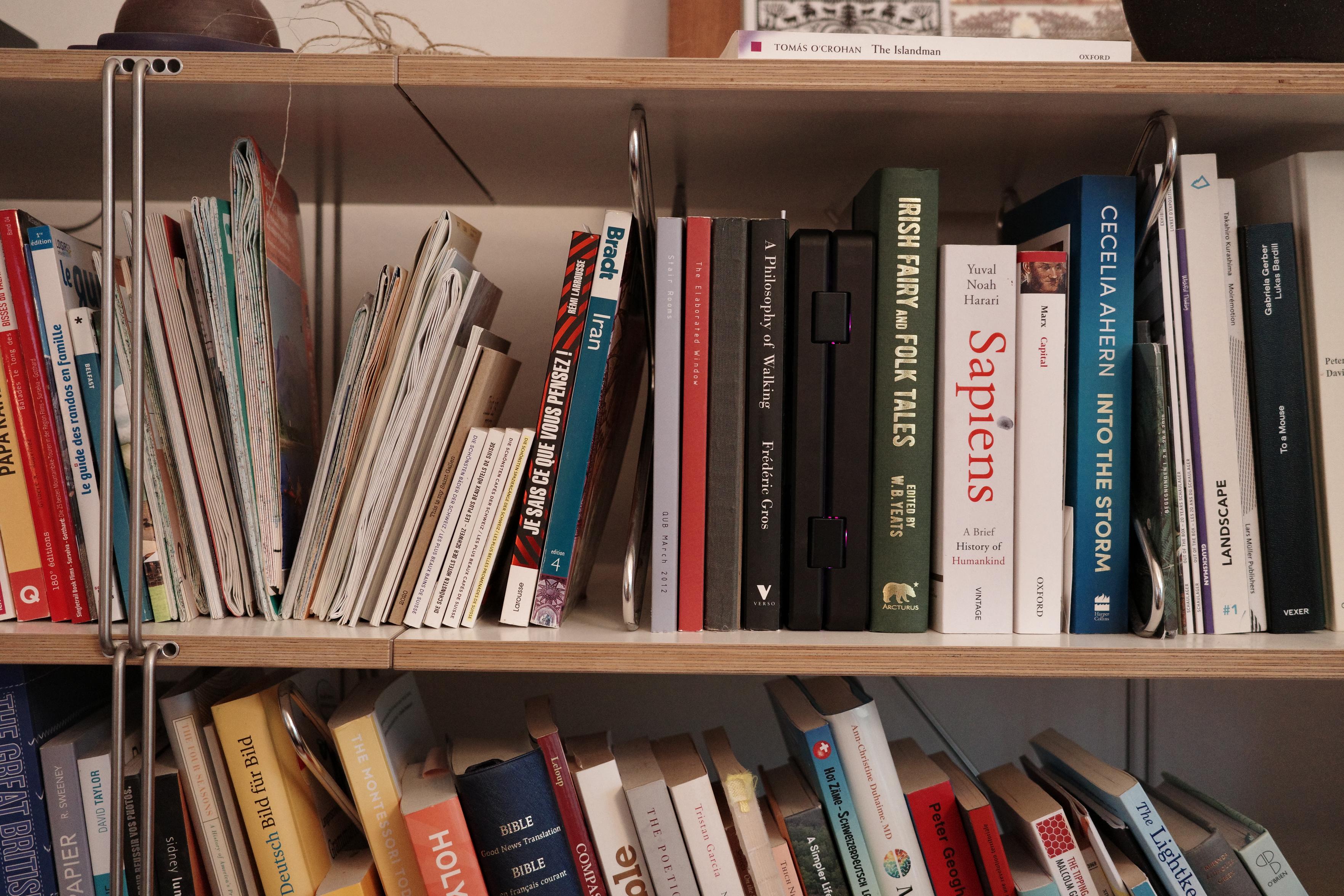 A bookshelf with many books, guides and map. In the the middle a pocket reform computer is folded and looks like a book edge.