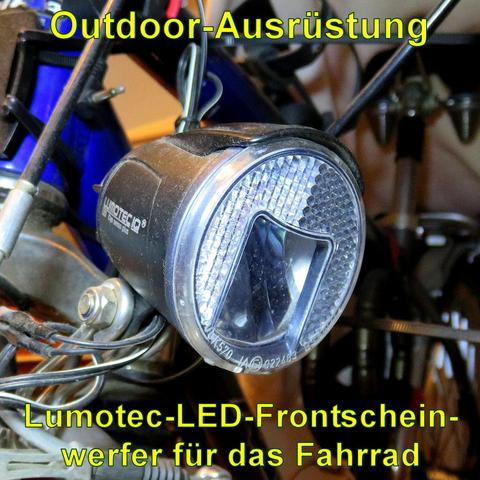 Ein Lumotec LED-Frontscheinwerfer der Marke Busch & Müller, Modell IQ Cyo Premium T senso plus, ist an einem Fahrrad montiert. Der Scheinwerfer hat ein robustes, schwarzes Gehäuse mit integriertem Reflektor um die LED-Linse. Er ist an der Gabel des Fahrrads befestigt und mit Kabeln verbunden, die wahrscheinlich zu einem Dynamo führen. Das Licht sorgt für starke Ausleuchtung bei Dunkelheit und ist ideal für den Einsatz bei Nachtfahrten oder schlechten Sichtverhältnissen.