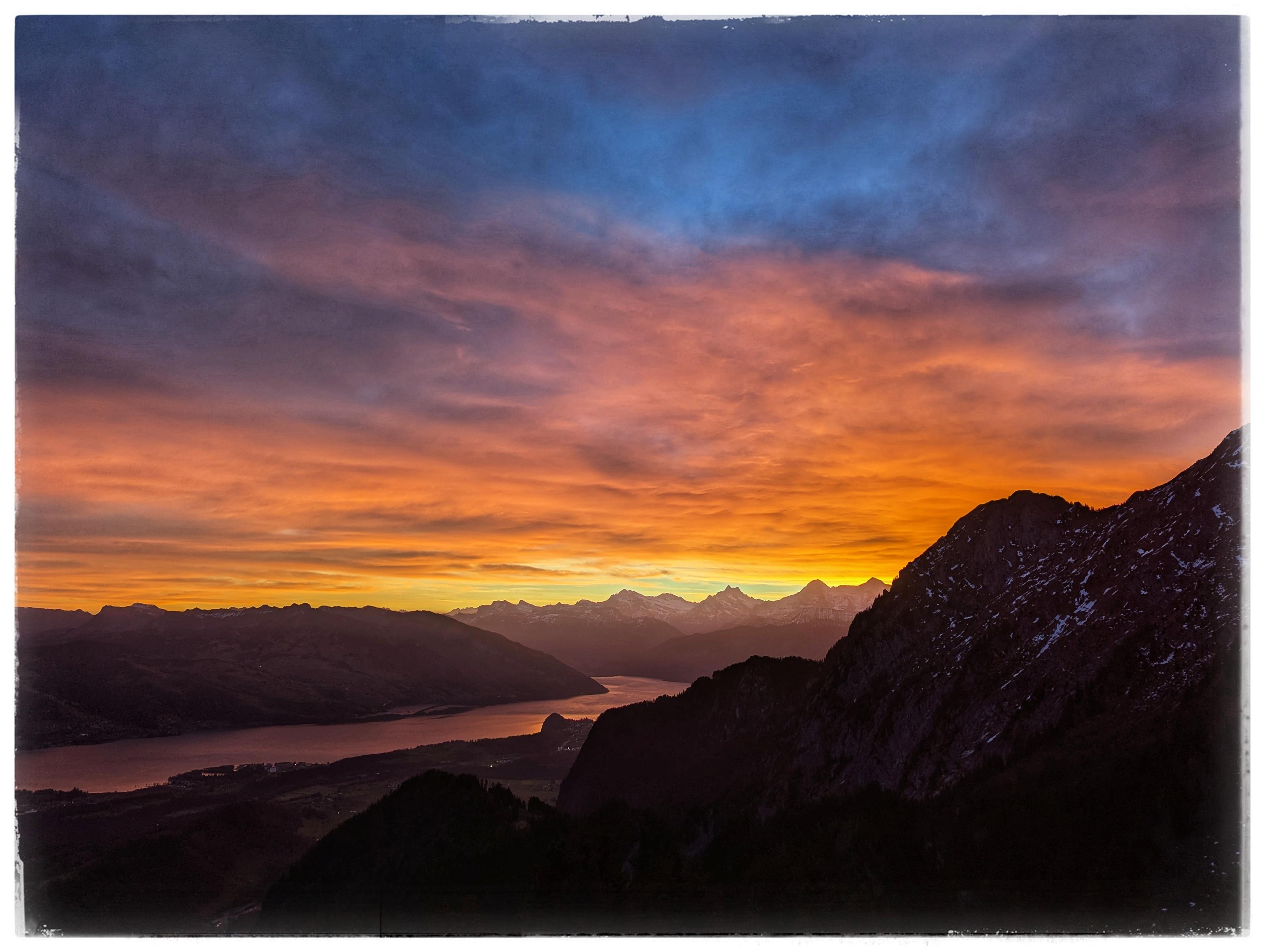 View from an alp, across a valley with a lake. Clouds colorful due to sunrise.