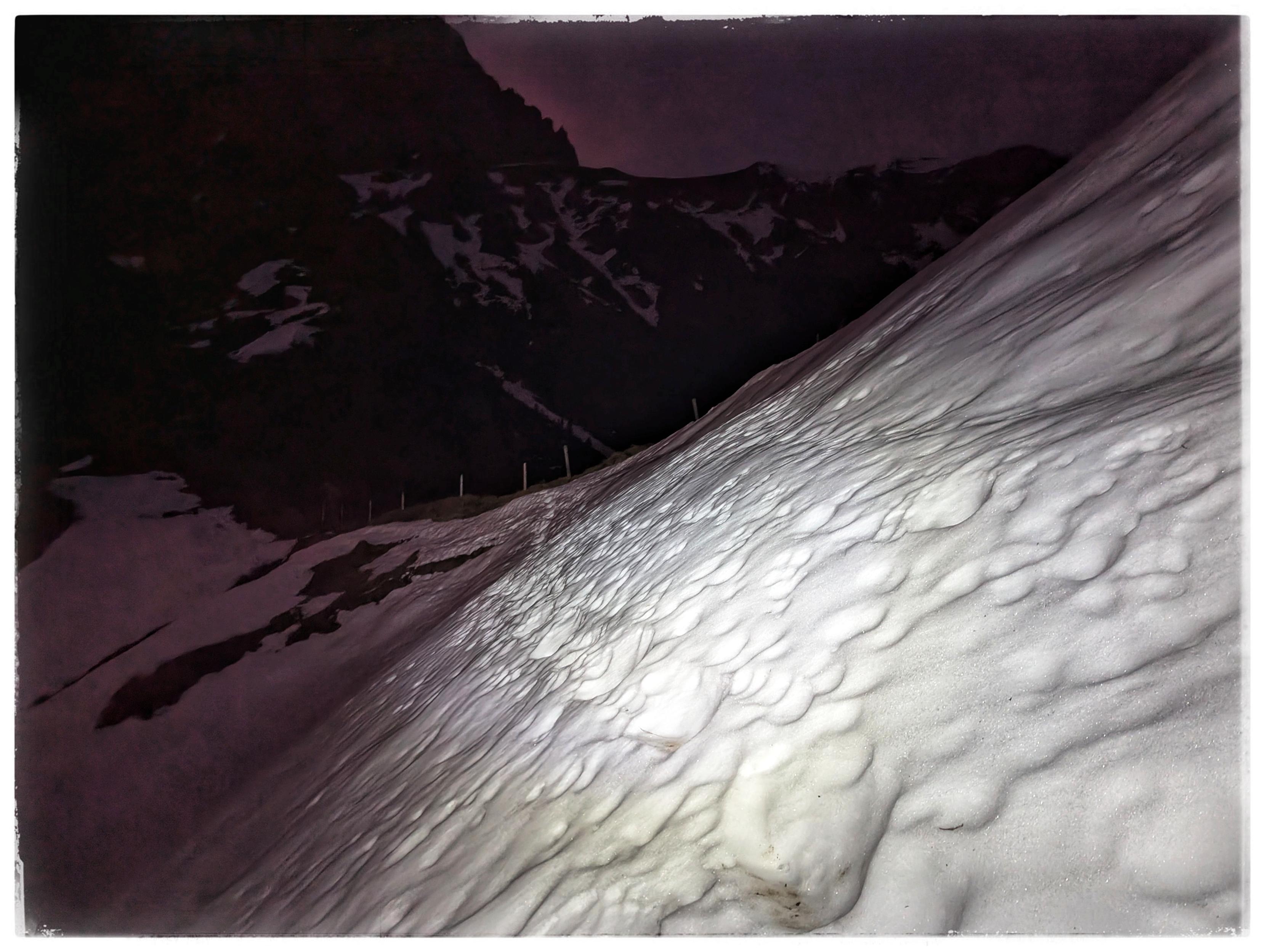 A steep lope with snow, some footprints visible in the snow.