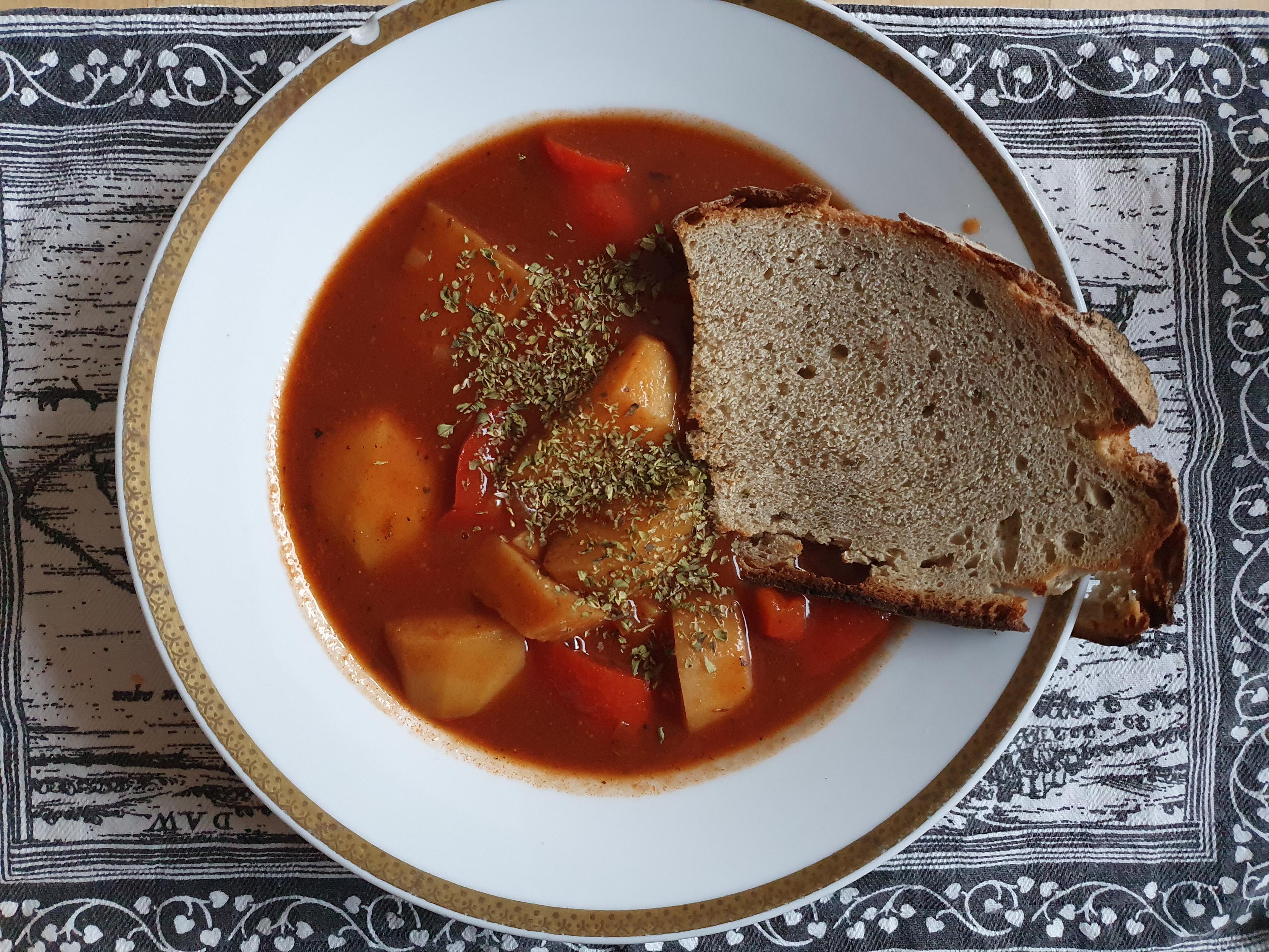 Kartoffelgulasch mit einer Scheiben Brot und Oregano im weißen Suppenteller