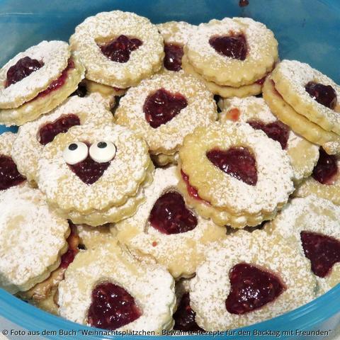 In einer hellblauen Kunststoffschüssel liegen Spitzbuben. Jeweils zwei Kekse sind mit Marmelade zusammengeklabt. Der obere Keks hat jeweils eine Herzöffnung in der Mitte und rote Marmelade scheint durch. Ein Keks hat zwei aufgeklabte Zuckeraugen.