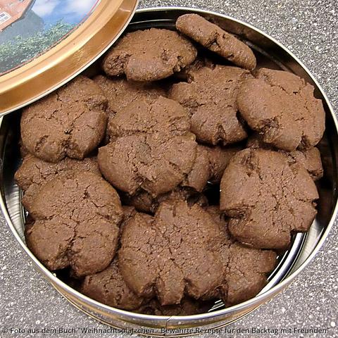 Auf der Küchenplatte steht eine Blechdose randvoll mit braunen Schmalzplätzchen. Die Ränder sind unregelmäßig dekorativ eingerissen durch das Plattdrücken vor dem Backen.