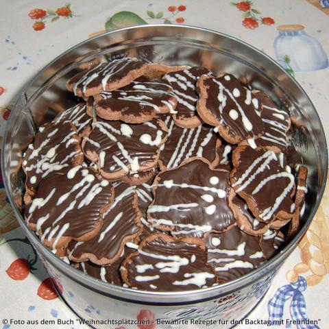 Anis-Schokoladen-Sterne in der Dose. Die Kekse sind braun, haben dunkelbraune Glasur und ein Muster aus hellbraunen und weißen Schokoladen-Strichen und -Punkten.