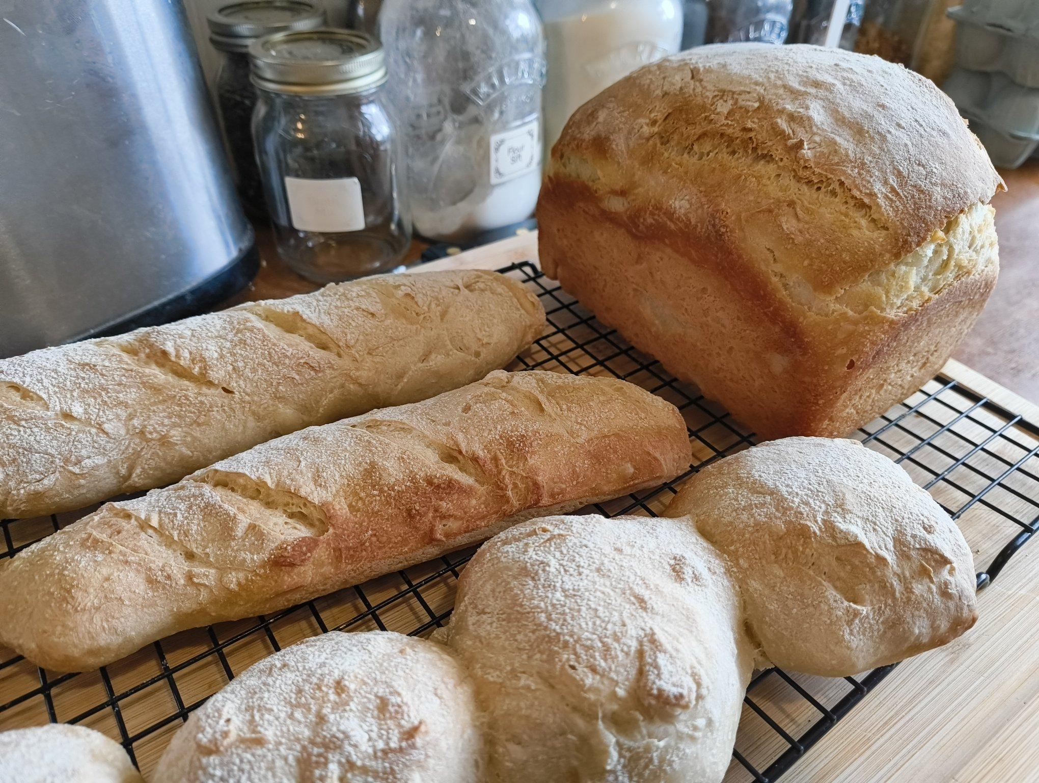A cooling rack with a sandwich loaf, two batons, and some burger buns.