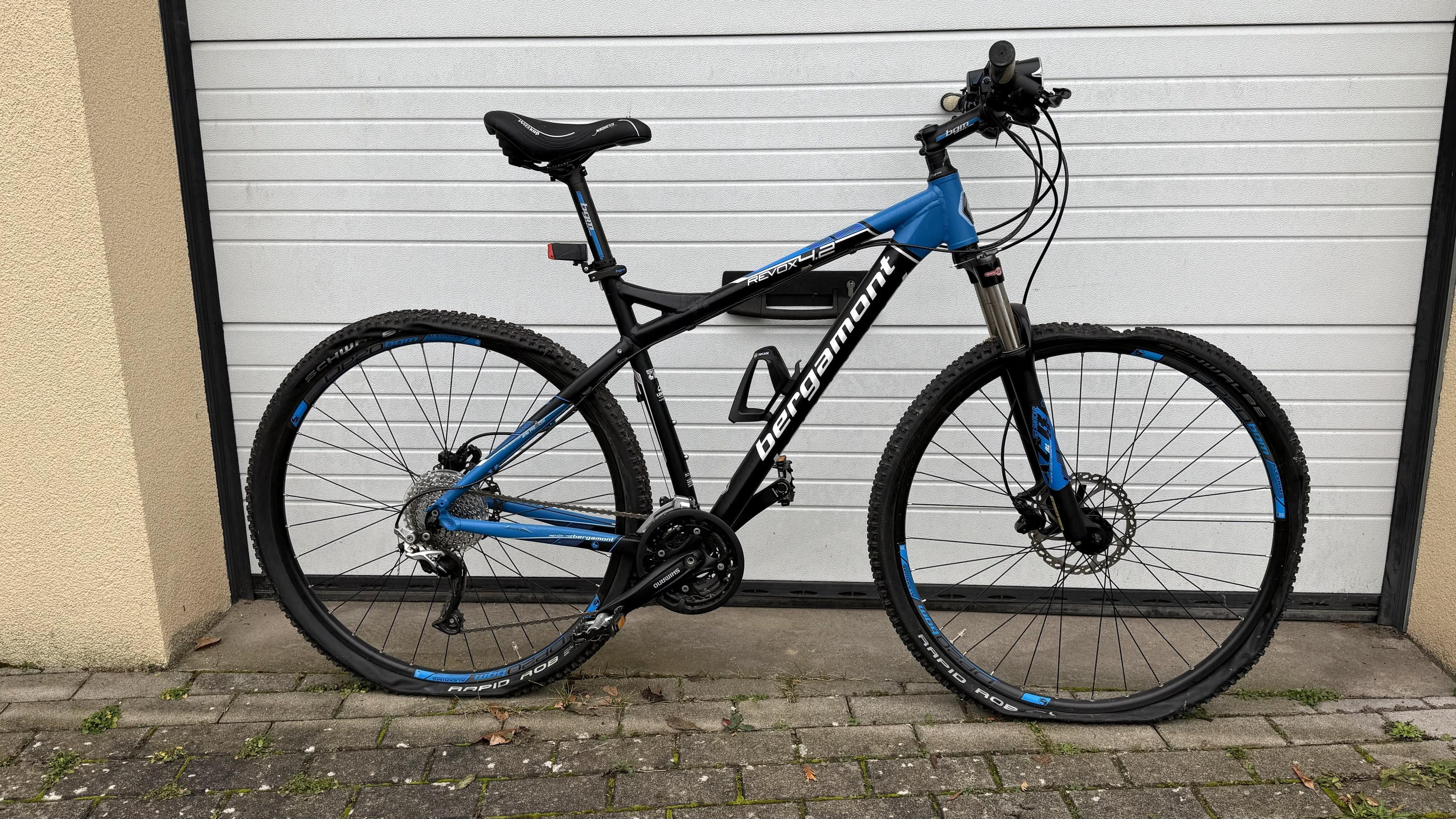 Ein schwarzes und blaues Mountainbike mit Full-Suspension steht vor einer Garage.