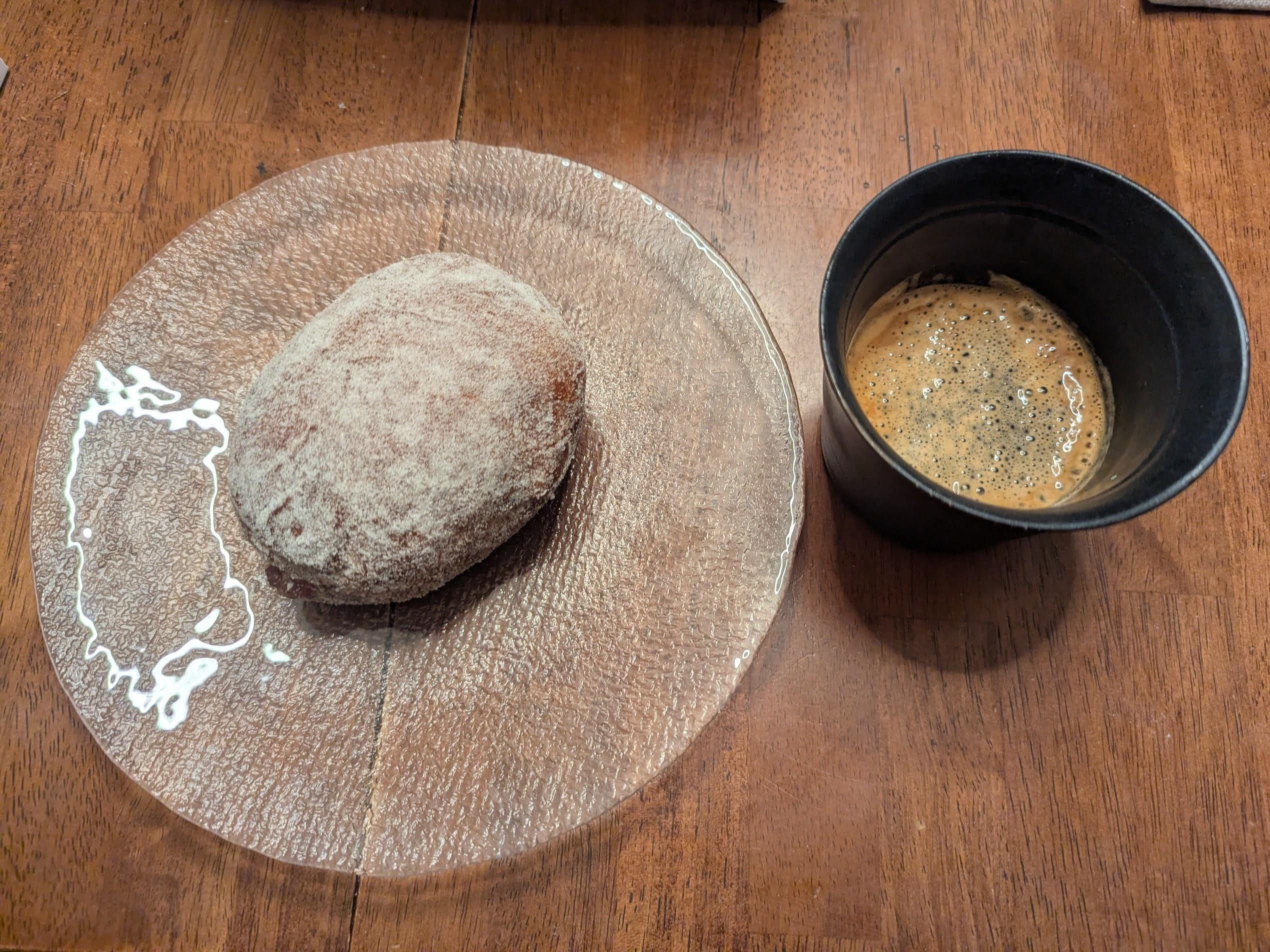 Rosehip paczki on a plate next to a black handleless mug with espresso on a table