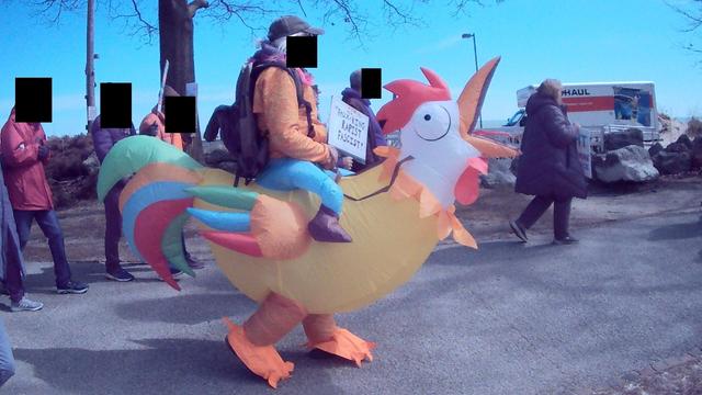 inflatable chicken costume worn by a man marching in the No Kings 3 protest with others in front of a blue sky