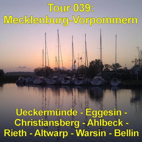 Kleiner Hafen mit mehreren Segelbooten, die nebeneinander am Steg liegen. Die hohen Masten ragen schlank in den Himmel und spiegeln sich im ruhigen Wasser. Das Gewässer wirkt glatt mit sanften Wellen. Im Hintergrund zeichnen sich Bäume und niedrige Gebäude als dunkle Silhouetten ab. Der Himmel leuchtet in warmen Orange- und Rosatönen nahe dem Horizont und geht nach oben in ein kühles Blau über. Die Szene zeigt eine Abendstimmung kurz nach Sonnenuntergang mit ruhiger, stiller Atmosphäre.