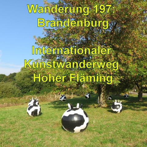 Skulpturen, die schwarz-weiß gefärbten Kuhflecken nachempfunden sind, verteilen sich auf einer grünen Wiese unter einem Baum. Sonnenschein und blauer Himmel ergänzen die Szene.