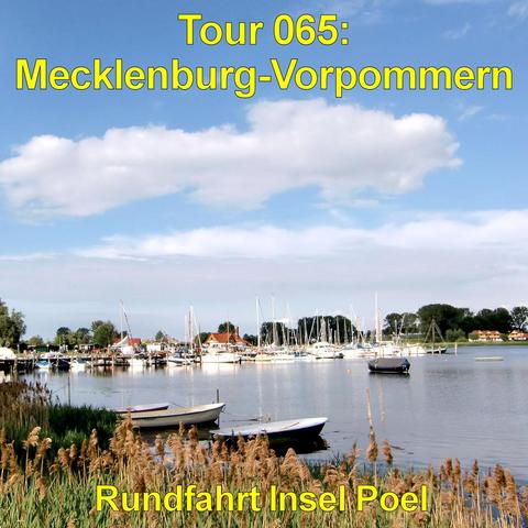 Kleiner Hafen mit zahlreichen Segelbooten, die dicht nebeneinander an Stegen liegen. Ihre Masten ragen schlank in den blauen Himmel mit großen, weißen Wolken. Im Vordergrund stehen zwei kleine Ruderboote im ruhigen Wasser, umgeben von Schilf mit hohen, braunen Halmen. Das Wasser wirkt glatt und spiegelt Boote und Himmel leicht wider. Am gegenüberliegenden Ufer stehen niedrige Gebäude mit roten und hellen Dächern, dahinter eine Reihe von Bäumen. Die Szene vermittelt eine ruhige, maritime Atmosph…