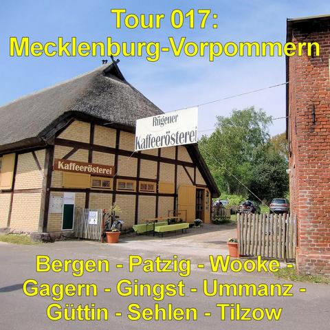 Traditionelles Fachwerkhaus mit hellem Mauerwerk und dunklen Holzbalken steht an einer kleinen Straße. Das Gebäude besitzt ein hohes Reetdach mit leicht geschwungener Form. An der Fassade hängen Schilder, vor dem Eingang stehen Bänke und Pflanzkübel. Ein niedriger Holzzaun begrenzt das Grundstück. Rechts daneben befindet sich ein rotes Backsteingebäude. Im Hintergrund sind einige parkende Autos und Bäume zu sehen. Der Himmel ist hell mit leichter Bewölkung. Die Szene wirkt ländlich und gepflegt.