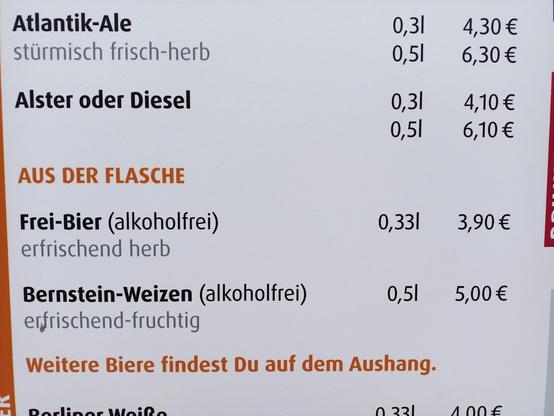Zu sehen ist ein Ausschnitt einer Getränkekarte mit Bierangeboten. Aufgeführt sind Atlantik-Ale, Alster oder Diesel sowie alkoholfreies Frei-Bier und Bernstein-Weizen. Daneben stehen Größen wie 0,3 l, 0,5 l und 0,33 l mit Preisen zwischen 3,90 € und 6,30 €. Ein orangefarbener Hinweis lautet: „Weitere Biere findest Du auf dem Aushang.“