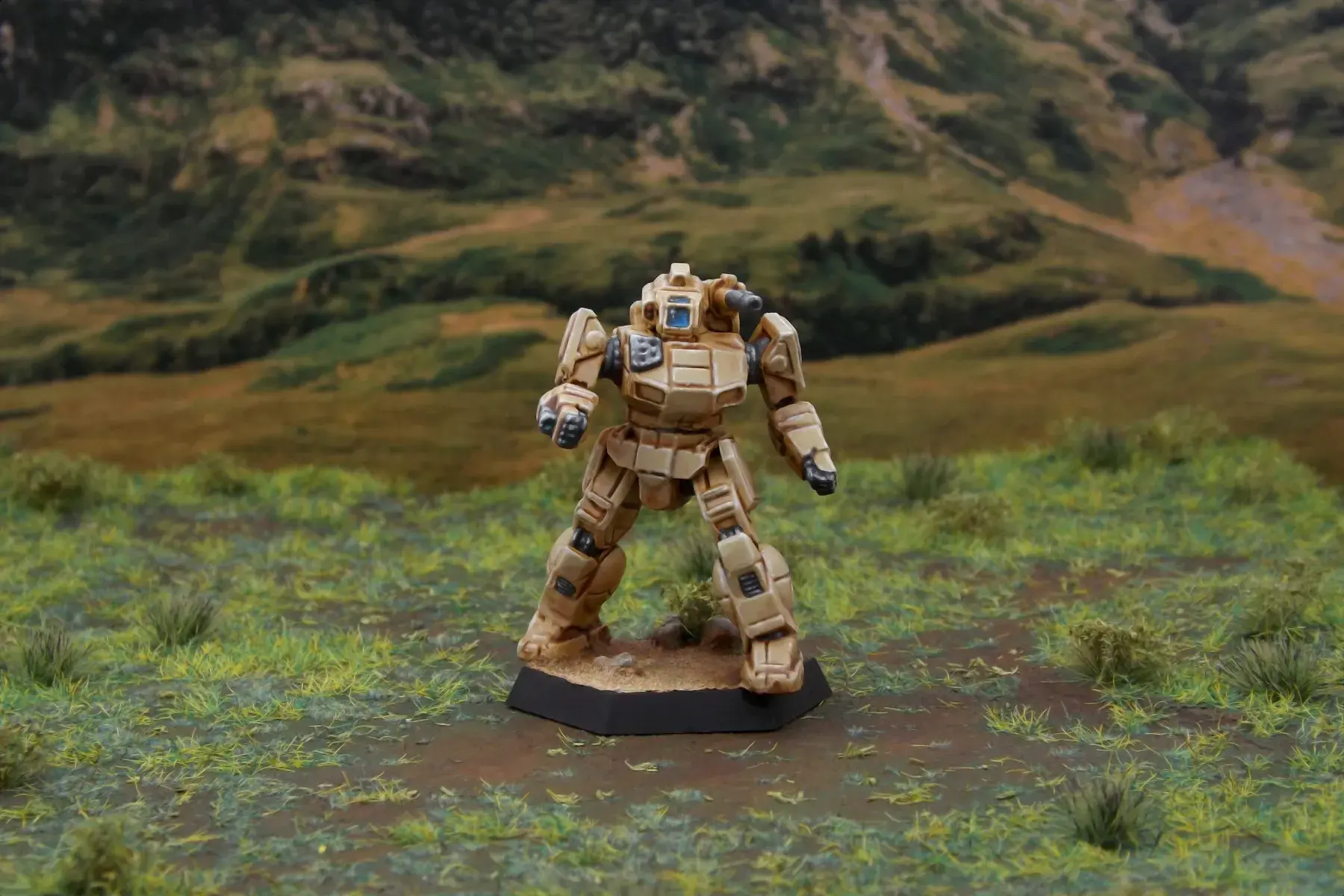 A painted miniature of a Shadow Hawk 'Mech.  It is tan and the cockpit glass is blue.  The miniature is photographed on grassy terrain.