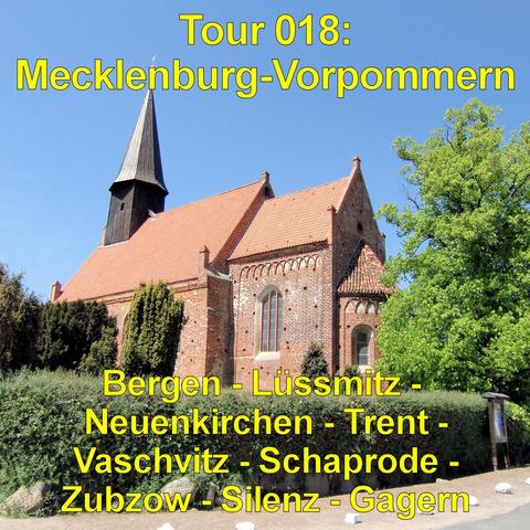 Backsteinkirche mit rotem Ziegeldach steht unter klarem, blauem Himmel. Der Bau besitzt spitz zulaufende Giebel und schmale, hohe Fenster mit hellen Rahmungen. Ein dunkler, hölzerner Turm mit steilem, spitzem Dach erhebt sich über dem Kirchenschiff. Die Fassade zeigt dekorative Zierbögen aus Backstein. Vor der Kirche verläuft eine niedrige Hecke, daneben steht ein großer, grün belaubter Baum. Der Vorplatz ist hell und offen gestaltet. Die Szene vermittelt den Eindruck einer historischen Dorfkir…