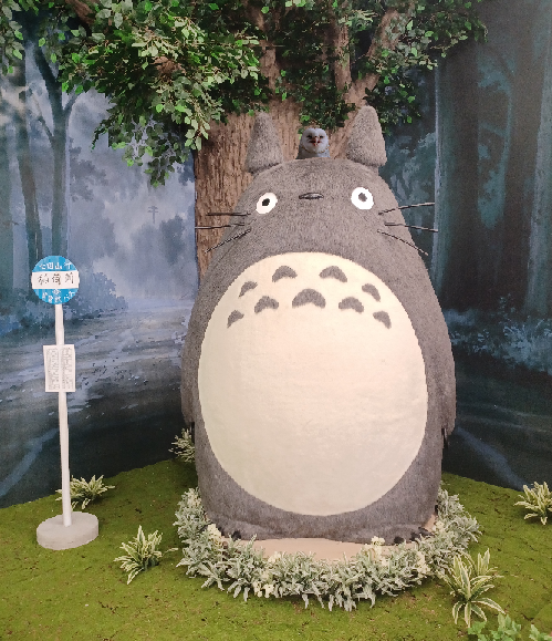 Smiling barn owl edited smiling from behind Totoro's head and between his ears at a photo op display at the Studio Ghibli Donguri Republic pop up in Torrance, California.