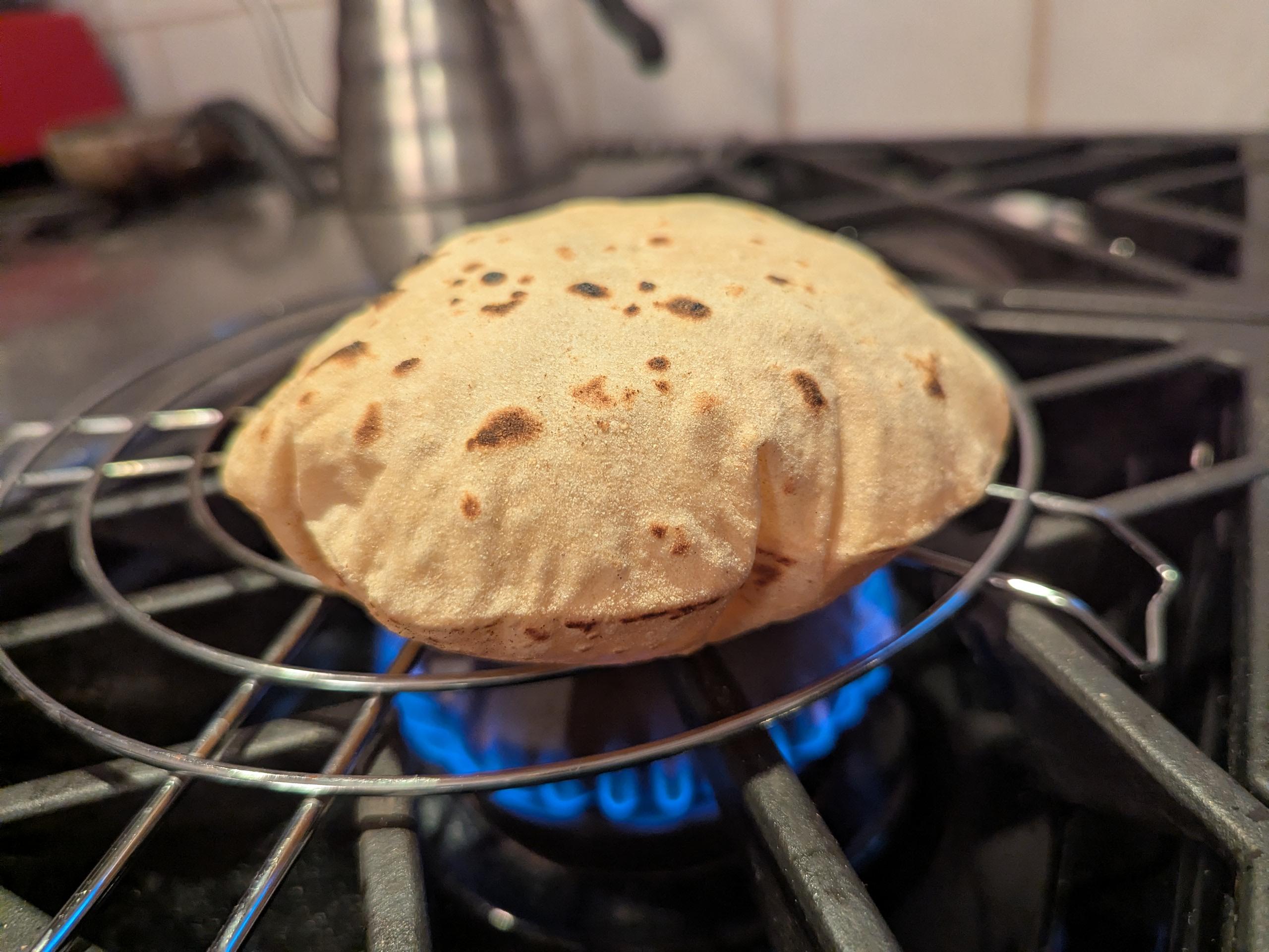 A fresh griddled wheat roti puffing up as it's held over a gas burner