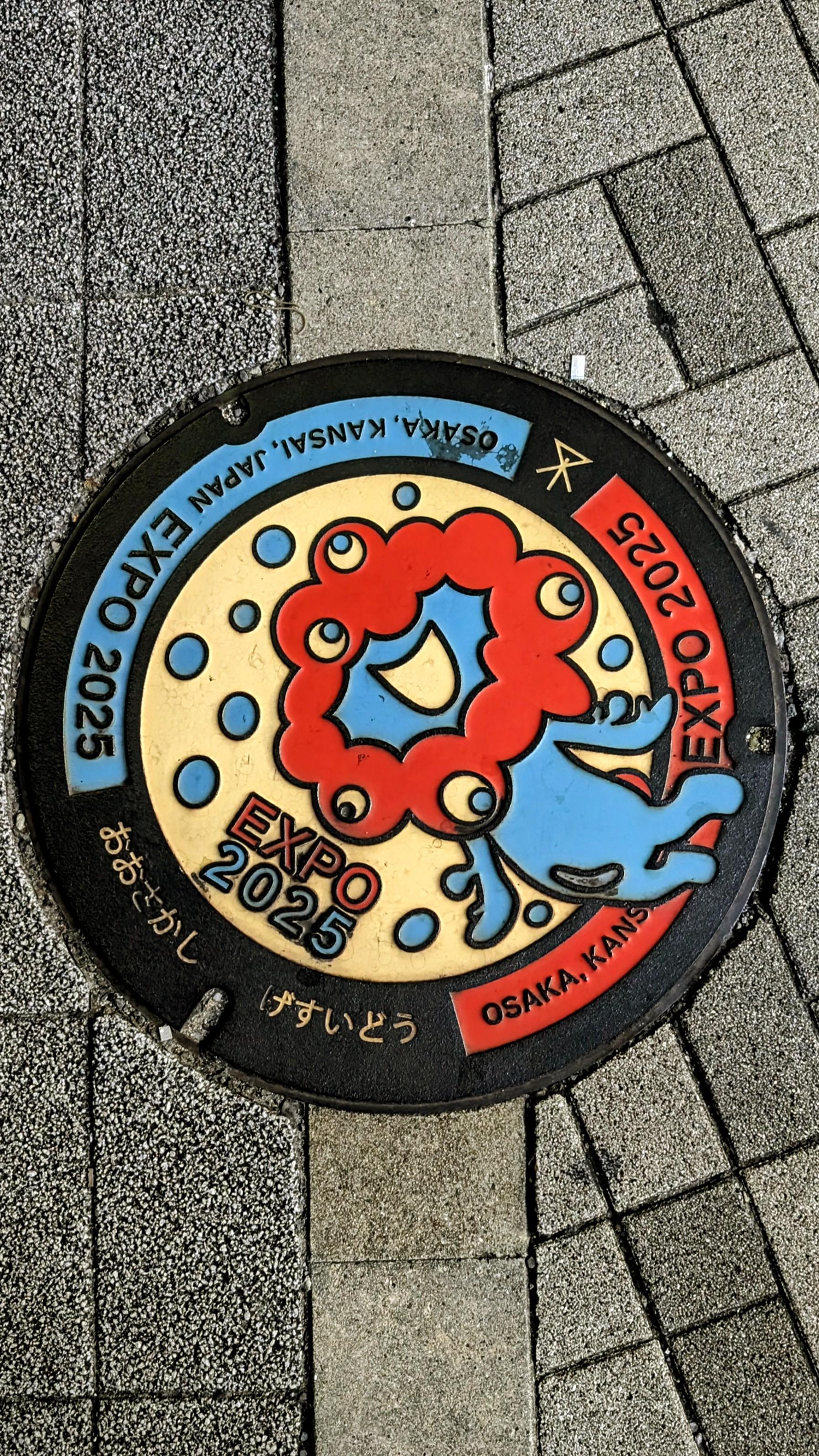 Colour photo of a very colourful manhole cover in Osaka, Japan, advertising the EXPO 25 there.