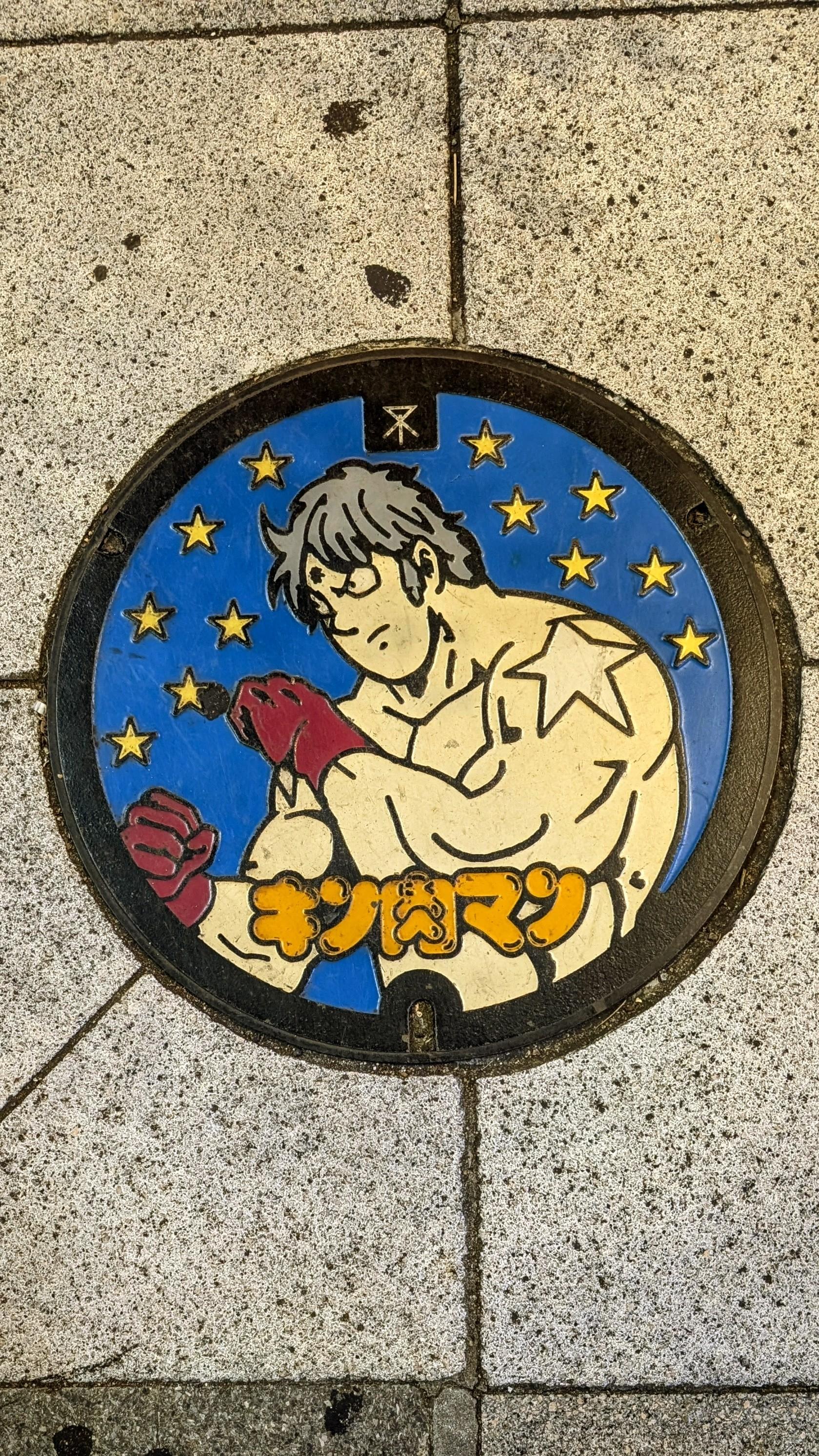 Colour photo of a very colourful manhole cover in Osaka, Japan. A male manga character?