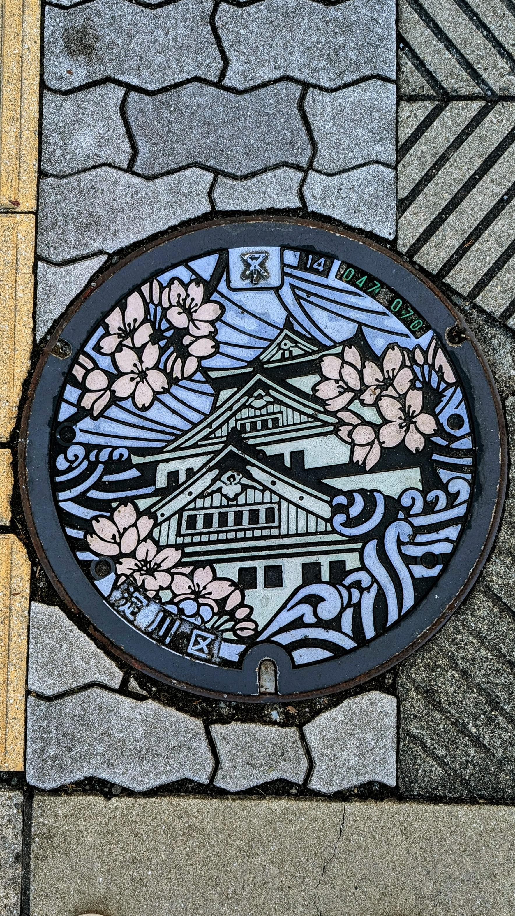 Colour photo of a very colourful manhole cover in Osaka, Japan of a temple.