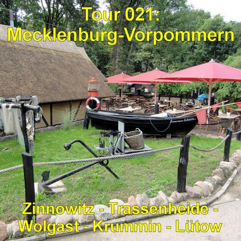 Gemütliche Szene in maritimem Stil: Im Vordergrund liegt ein großer schwarzer Anker auf einer kleinen Rasenfläche, eingefasst von einem niedrigen Steinrand und Holzpfosten mit Tauwerk. Dahinter steht ein traditionelles Reetdachhaus. Vor dem Gebäude befindet sich ein Außenbereich mit zahlreichen Tischen und Stühlen, beschattet von großen roten Sonnenschirmen. Ein schwarzes Holzboot mit Rettungsring ist dekorativ an Land platziert und unterstreicht das Küstenflair. Hohe Bäume im Hintergrund sorge…