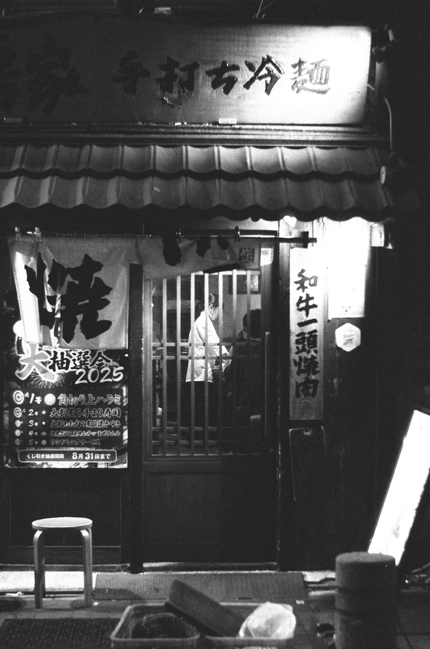 Black and white 35mm film photo of a chef preparing food in a restaurant kitchen in Tokyo, Japan. Photo taken at night.