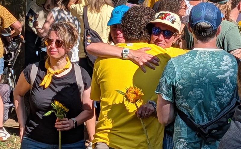 People hugging while holding sunflowers at memorial for Laura Gag