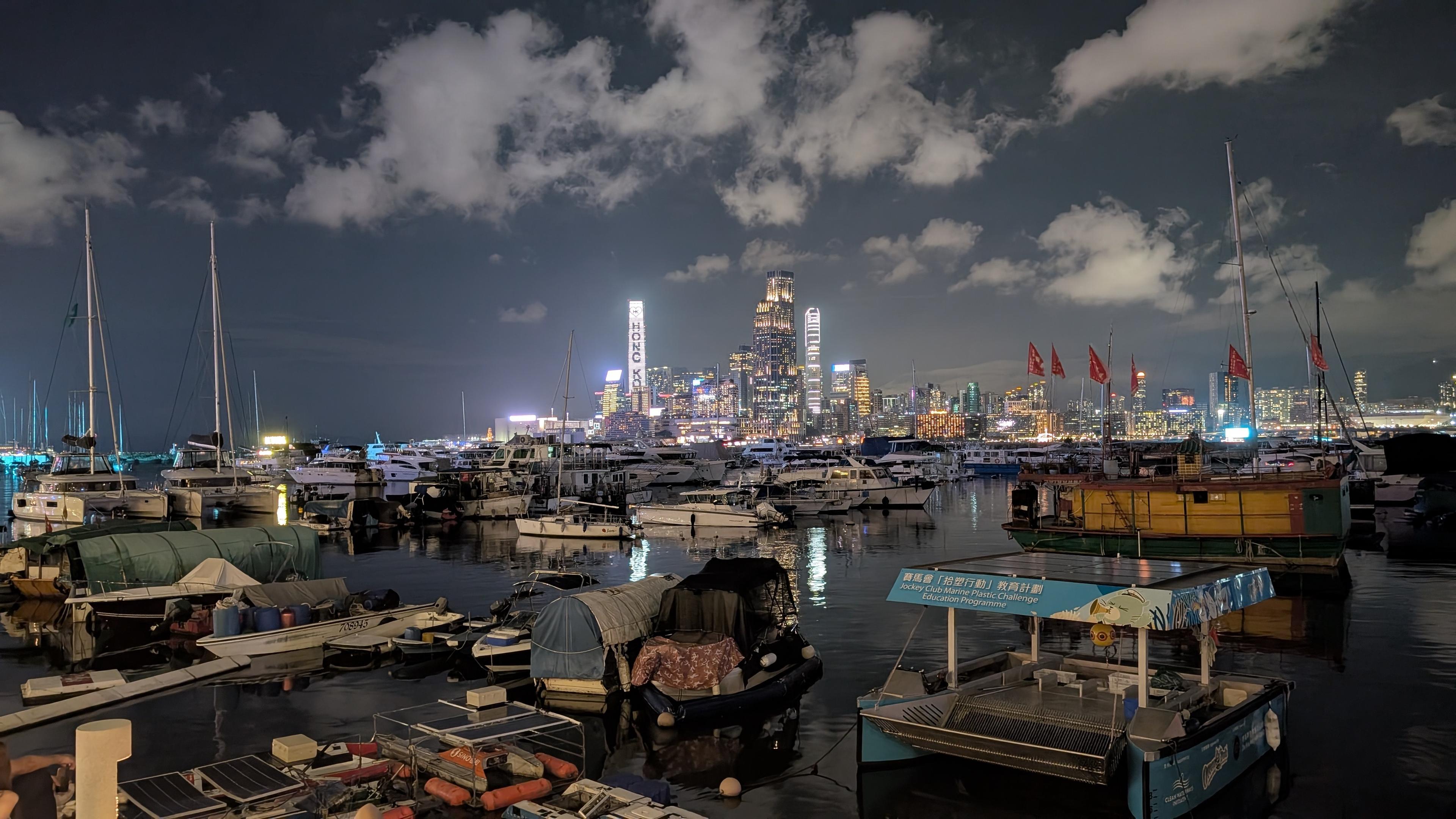 Colour photo of a view across the harbour, North Point, Hong Kong at night.
Image shows boats of all sizes moored in the harbour. In the background are a section of modern high rise buildings.