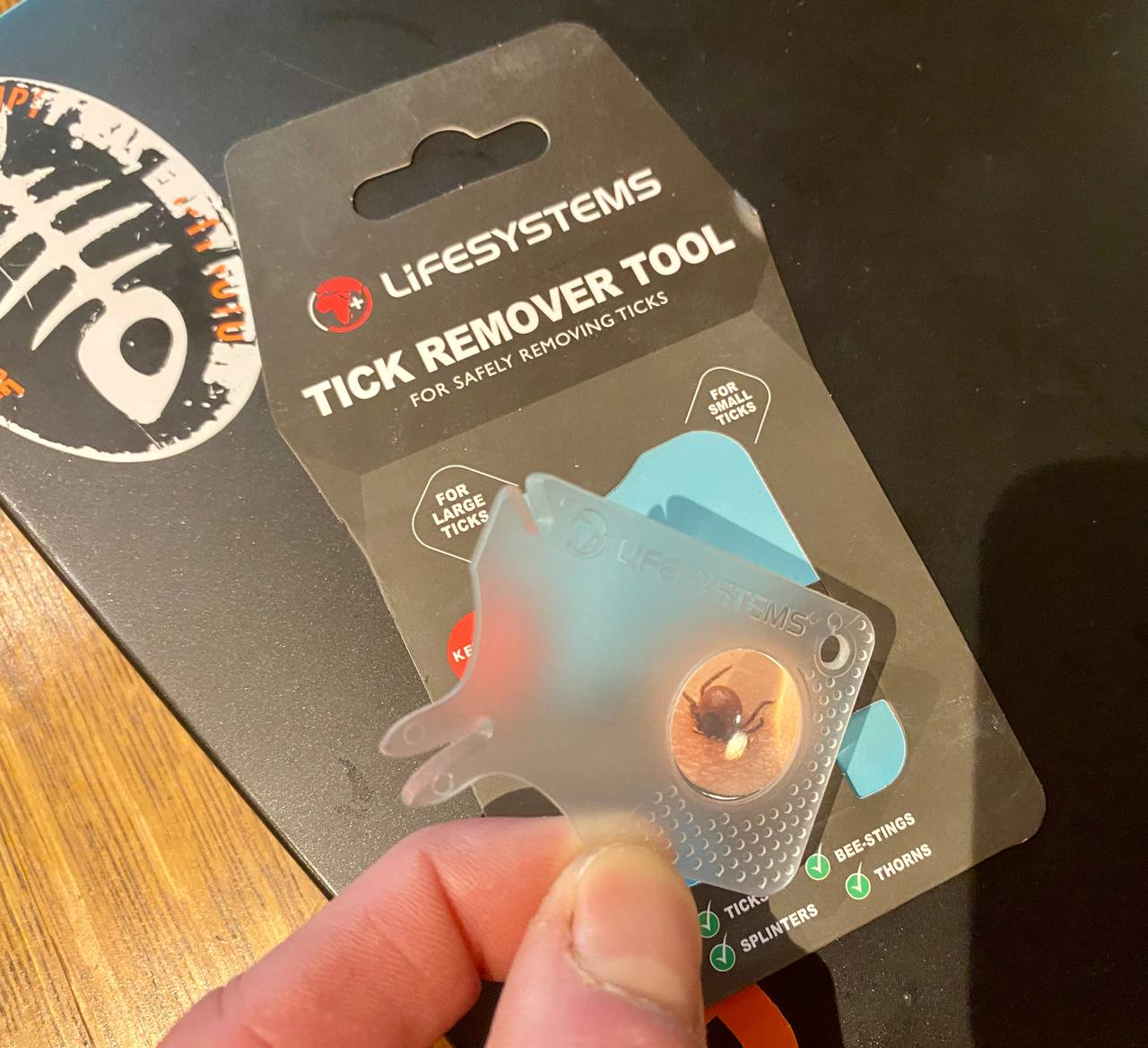 Lifesystems tick removal tool. A molded plastic card with two sizes of tick removal fingers, and a little magnifying glass. It's absolutely brilliant: cheap, easy to carry and truly works on both tiny ticks and SUV sized ones.

I paid 30 Danish kroner for it. Seems prices are a bit opportunistic between 25 and 70 DKK depending on the store. It's worth it though as this is the only tool I've ever used that consistently just pops out the entire tick without the head breaking off and staying in the skin or it taking some seconds in which the tick pukes out its guts (incl. borrelia) in your body.