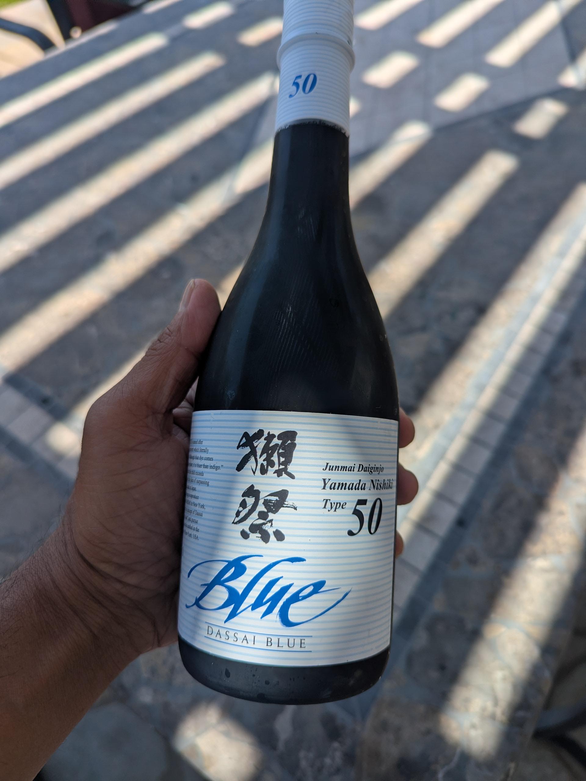 Hand holding a 375 mL bottle of Dassai Blue 50 sake