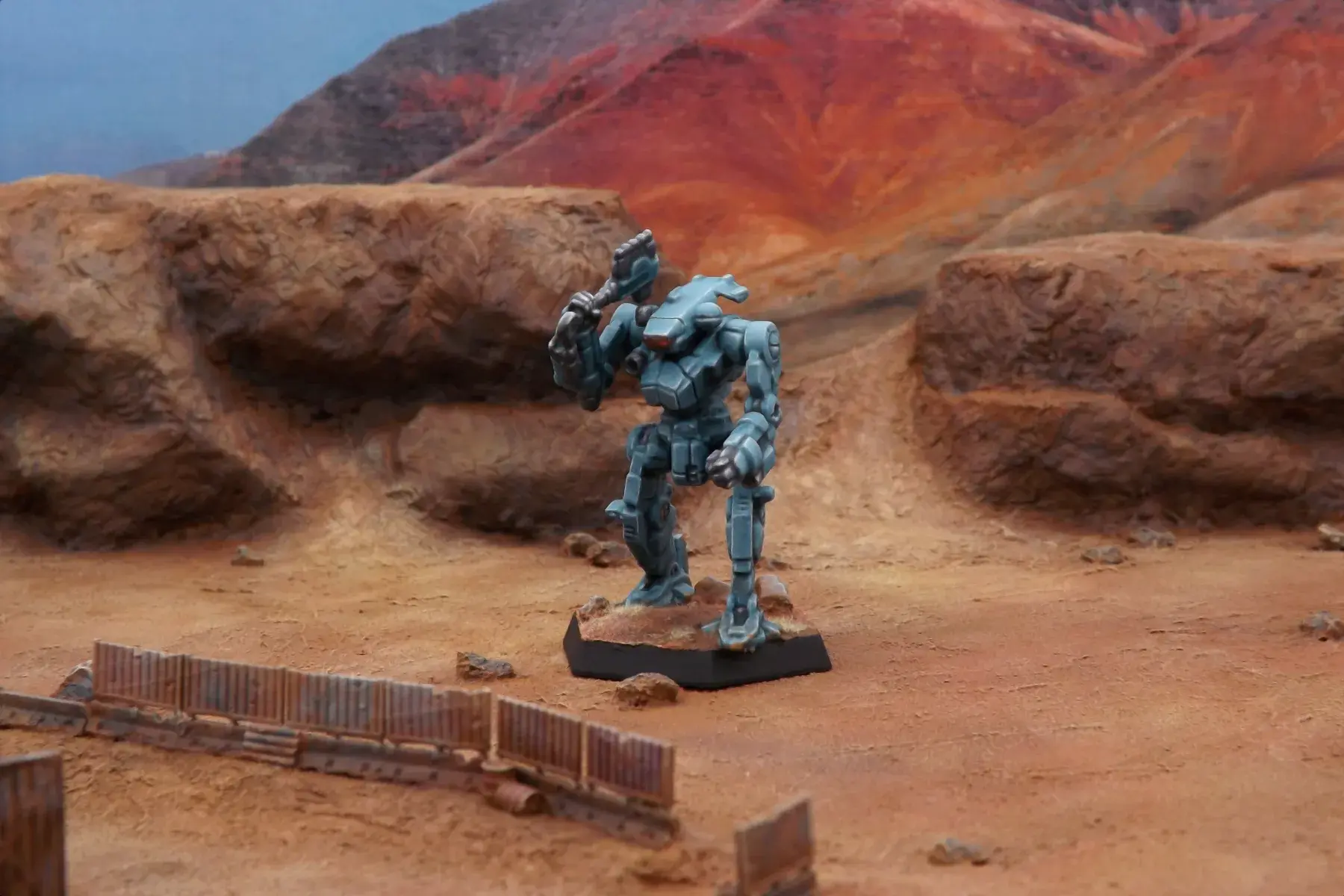 A painted miniature of a Hatchetman 'Mech.  It is greenish blue and the cockpit glass is red.  The miniature is photographed on desert terrain.