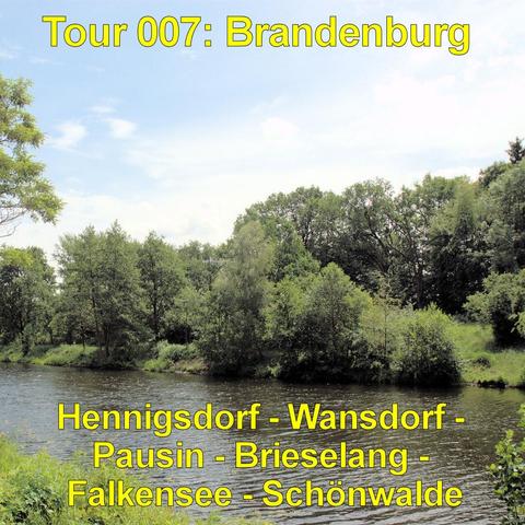 Ruhiger Fluss mit leicht bewegter Wasseroberfläche im Vordergrund. Am gegenüberliegenden Ufer wächst eine dichte Reihe aus Bäumen und Sträuchern in verschiedenen Grüntönen. Einige Bäume neigen sich leicht über das Wasser, ihre Kronen bilden ein geschlossenes Blätterdach. Das Ufer ist grasbewachsen und stellenweise flach abfallend. Der Himmel darüber ist hellblau mit vereinzelten, weichen Wolken. Die Szene vermittelt eine naturnahe Flusslandschaft ohne sichtbare Bebauung.