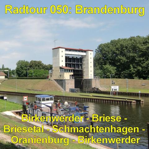 Ein breiter Kanal mit ruhigem Wasser verläuft durch eine gepflegte Grünanlage. Am Ufer steht ein mehrstöckiges, rechteckiges Gebäude mit heller Fassade und vielen Fenstern. Davor führt eine Brücke oder Schleusenanlage über das Wasser, mit Metallgeländern und technischen Aufbauten. Ein kleines Arbeitsboot mit Ausrüstung liegt am Rand des Kanals. Die Böschungen sind mit Gras bedeckt und von Bäumen gesäumt. Mehrere Wege und Straßenlampen verlaufen entlang des Wassers.