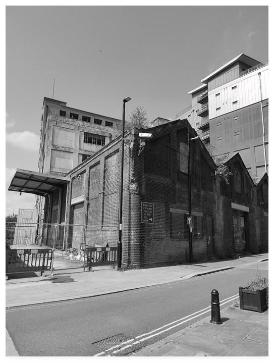 Black and white portrait photograph of a derelict old warehouse building with a modern apartment block behind.
