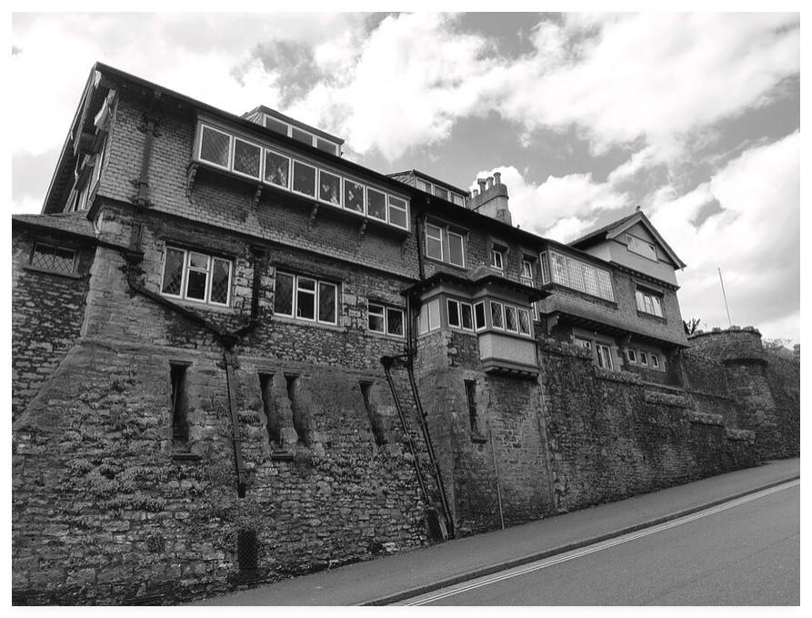 Black and white photograph of a large roadside residential property that has a slight castle like look to it.