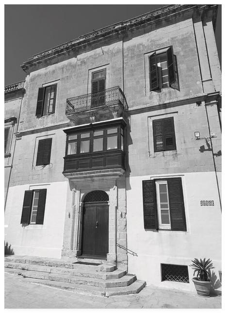 Black and white photograph of a 3 storey building in Malta with a balcony above an oriel window.