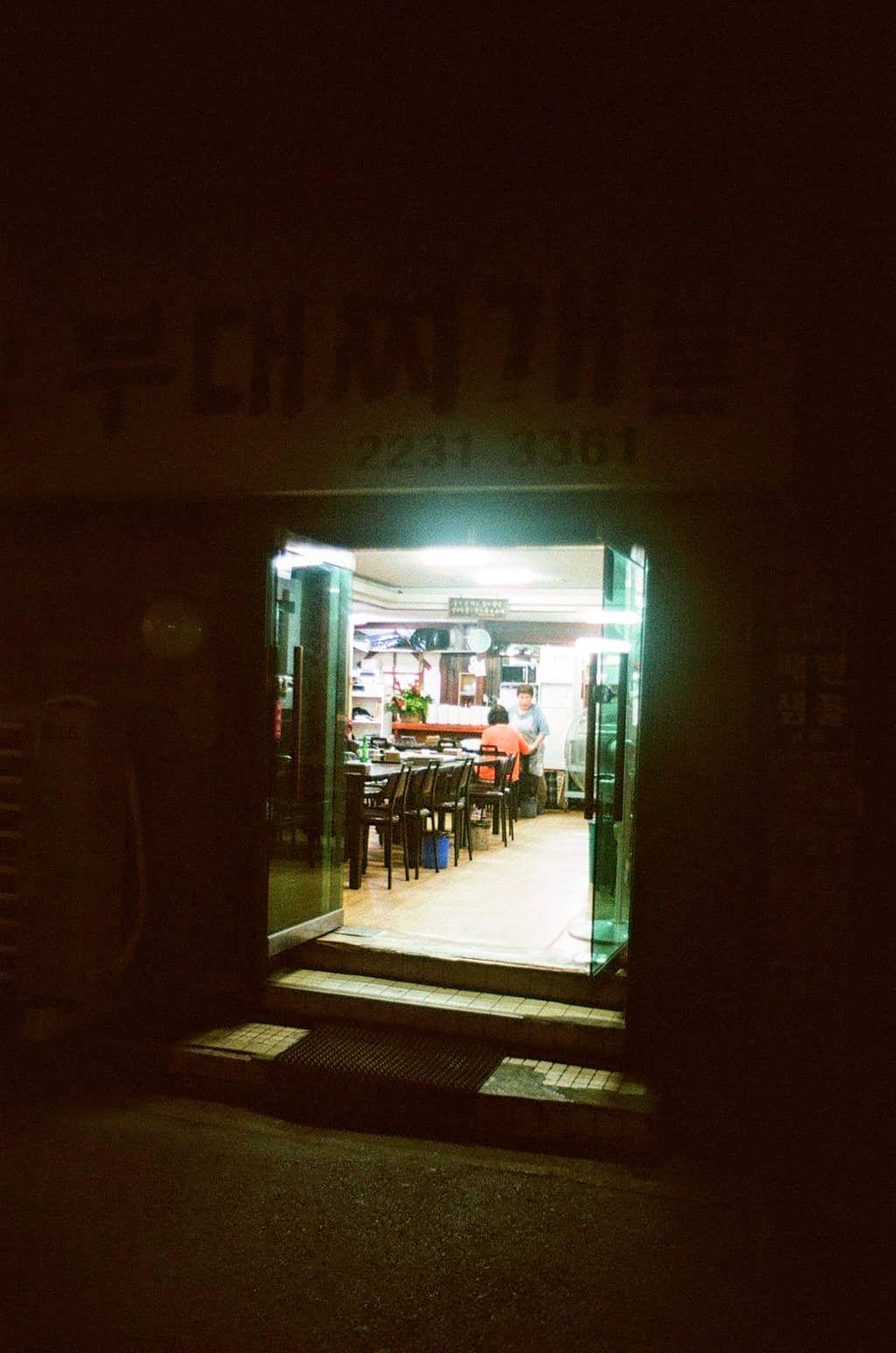 Colour 35mm film photo of a couple of ladies inside a restaurant having a chat. Taken at night from the street looking inside. I'm guessing they have had a busy night and have finally getting a break and a chat.
