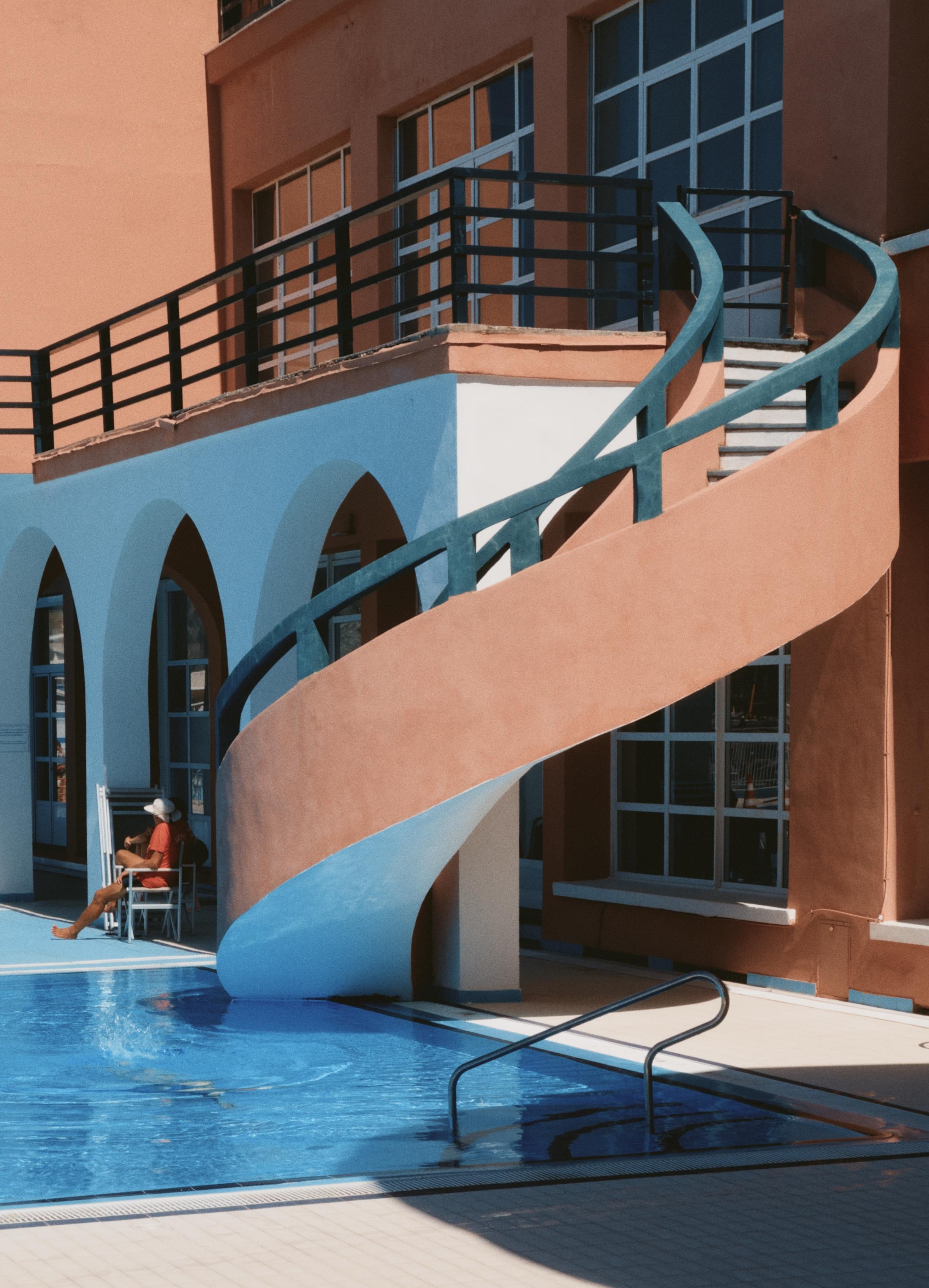 A photo of a pool with a spiral staircase, vintage resort style. Pastel colours. Sunny.