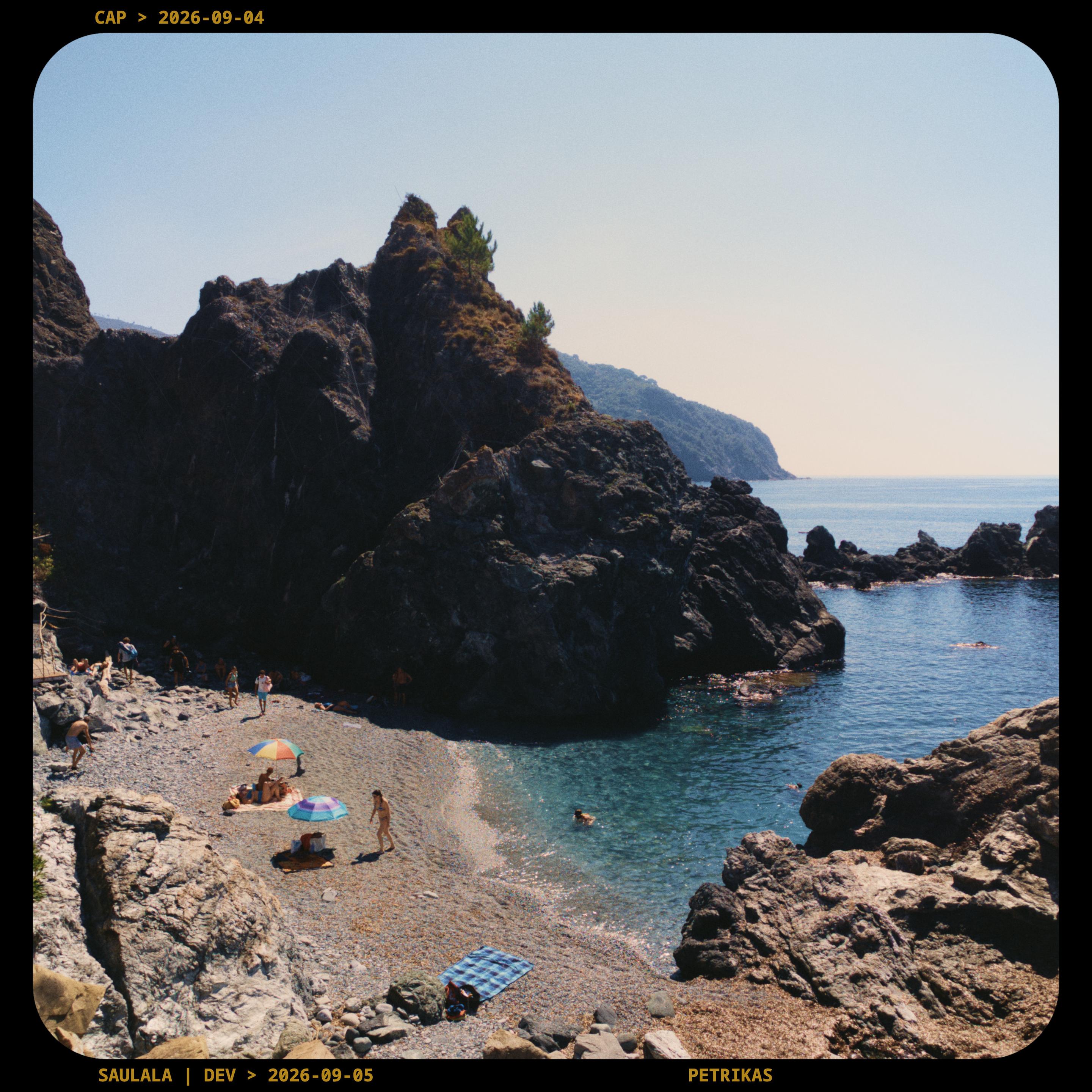 The image depicts a rugged, rocky coastline featuring a small, secluded cove with a pebbly beach.