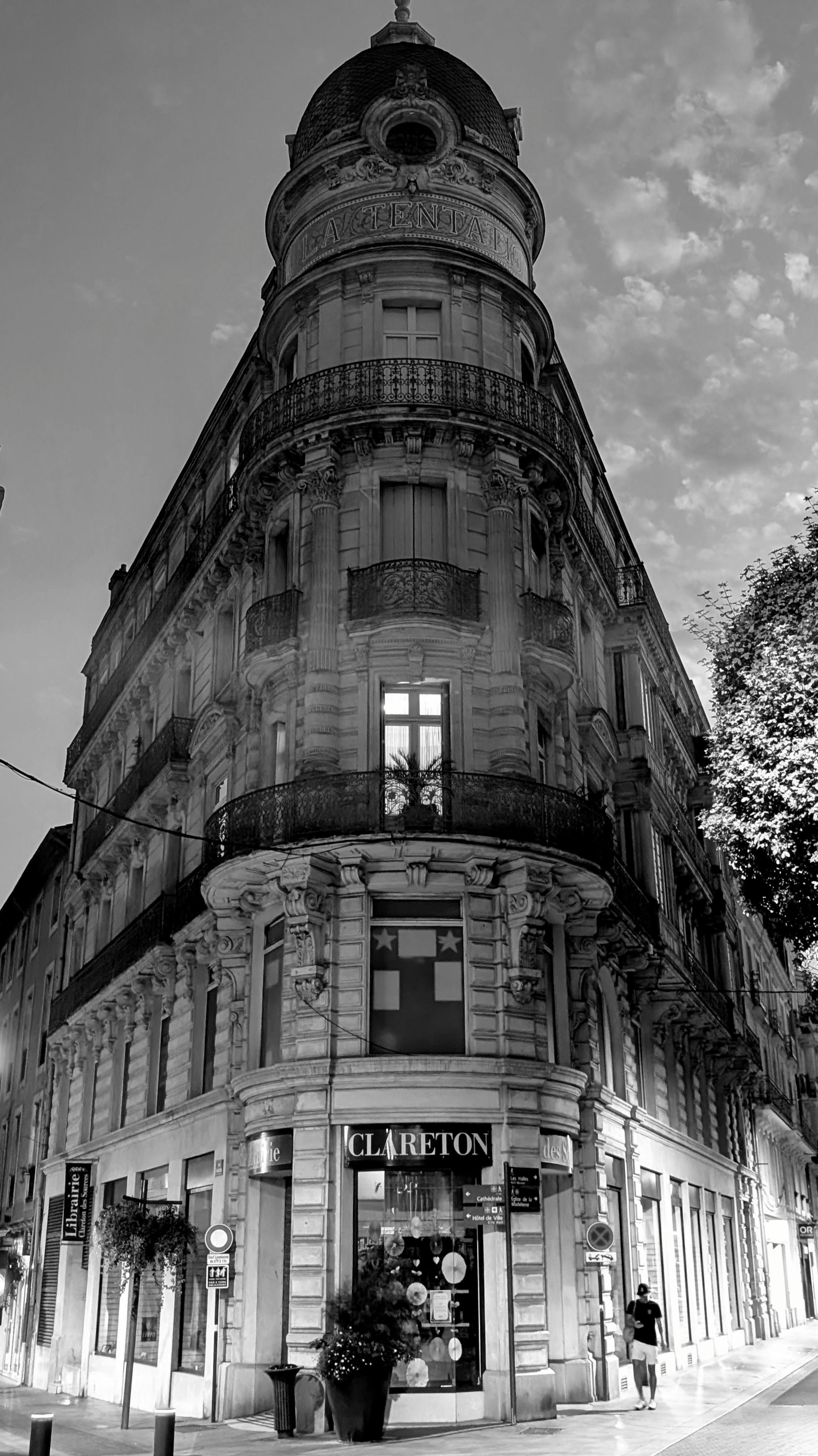 Black and white photo of a very elegant building in Béziers, France.
Image shows a grand building with a lone light on. A young man is walking by the building.
It's now dark and the street lights are shining on the street below.
Taken tonight on a wander.