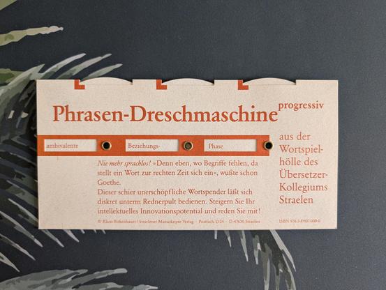 Eine beigefarbene Papp-Drehscheibe mit dem Titel „Phrasen-Dreschmaschine progressiv“ auf dunklem, gemustertem Hintergrund. Über drei Sichtfenster ist die Wortkombination „ambivalente Beziehungs-Phase“ eingestellt.