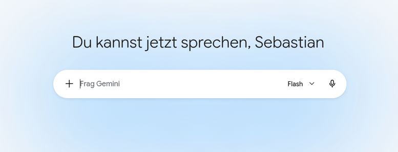 Ein Screenshot eines Ausschnitts der minimalistischen Web-Benutzeroberfläche von Google Gemini auf einem hellblau-weißen Verlaufshintergrund. Zentriert steht in serifenloser Schrift der Aufforderungstext „Du kannst jetzt sprechen, Sebastian“. Darunter befindet sich ein weißes, pillenförmiges Eingabefeld mit einem Plus-Symbol ganz links, dem grauen Platzhaltertext „Frag Gemini“ samt blinkendem Cursor, einem Dropdown-Menü für das Modell „Flash“ mit Pfeilsymbol und einem Mikrofonsymbol ganz rechts.