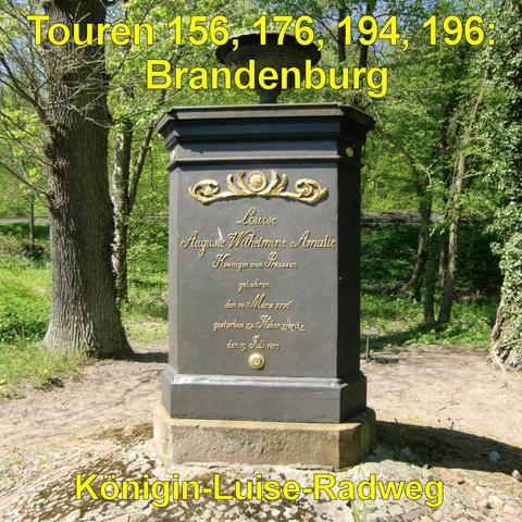 Dunkler, rechteckiger Gedenkstein aus Metall oder Stein auf einem Sockel, umgeben von Wald. Die Vorderseite ist mit goldfarbenen Verzierungen und einer Inschrift gestaltet. Oben befindet sich ein dekoratives Ornament mit geschwungenen Elementen. Der Stein steht auf einer gepflasterten Fläche, die von Erde und Laub umgeben ist. Hohe Bäume mit grünen Blättern spenden Schatten, im Hintergrund verläuft ein schmaler Weg durch das Gehölz. Das Denkmal wirkt gepflegt und freistehend inmitten der Natur.