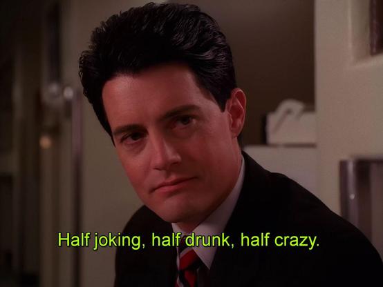 A medium close-up shot of a person with dark, wavy hair looking toward the camera. The person is wearing a dark suit jacket and a red tie. The background is a blurred indoor setting. Yellow text at the bottom of the image reads, "Half joking, half drunk, half crazy."